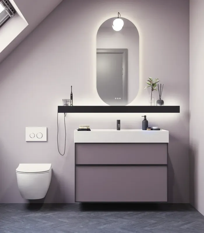 Badeværelse med skrå vægge inspiration, med badeværelsesmøbler i lilla med elegante rammefronter, flot ovalt spejl med lampe, smuk og praktisk hylde, samt lillamalet væg og gråt sildebensgulv, der giver et elegant og moderne udtryk.