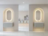 Stilfuld og moderne badeværelse inspiration med ovale spejle med lysstyring, stenvaske og vaskeskabe med fine og elegante riller i et minimalistisk design, badeværelset har en lys og luftig atmosfære med elegant belysning og raffinerede detaljer
