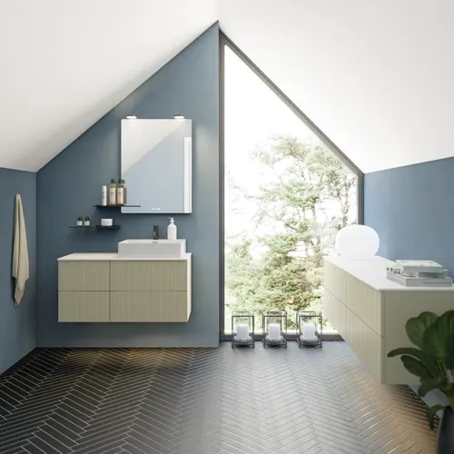 Badeværelse med skrå loft inspiration, beige badeværelsesmøbler med rifler, elegant bordplade samt firkantet bordstående håndvask, smukt firkantet spejl med stilfulde hylder, blå vægge, store vinduer og sort sildebensgulv giver et lyst og urban udtryk.