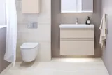 Lille badeværelse inspiration med vaskeskab og overskab over toilet i beige specialfarve, elegant spejlskab med integreret lys, de lyse farver og hvide gardin skaber en romantisk og feminin atmosfære.