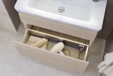 Lille badeværelse inspiration med vaskeskab og overskab over toilet i beige specialfarve, elegant spejlskab med integreret lys, de lyse farver og hvide gardin skaber en romantisk og feminin atmosfære.