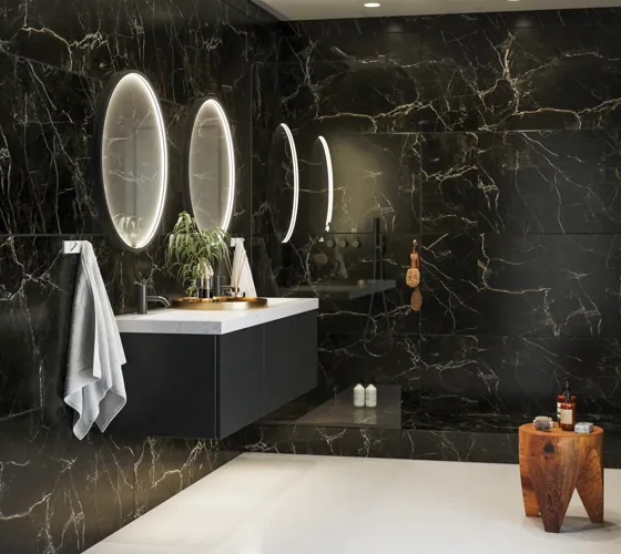 Elegant og moderne badeværelse inspiration med mørke marmorvægge, runde oplyste spejle med sort ramme, væghængt vaskeskab med dobbeltvask og en rummelig bruseniche
