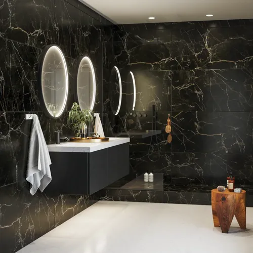 Elegant og moderne badeværelse inspiration med mørke marmorvægge, runde oplyste spejle med sort ramme, væghængt vaskeskab med dobbeltvask og en rummelig bruseniche