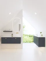 Elegant og moderne badeværelse inspiration med skrå loft, væghængte blå vaskeskab og underskabe, rund vask med messing armatur, oplyst spejl og naturligt lysindfald