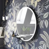 Badeværelse inspiration med mørkeblå vægpaneler, romantisk blomstret tapet, mørkeblåt vaskeskab med bløde former og et smukt rundt spejl med lys, der skaber et vintage udtryk
