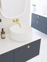 Elegant og moderne badeværelse inspiration med skrå loft, væghængte blå vaskeskab og underskabe, rund vask med messing armatur, oplyst spejl og naturligt lysindfald