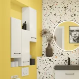 Lille badeværelse inspiration med hvide vaskeskab med sort greb og sort elegant håndvask, smukt rundt spejl med sort kant, forskudt placerede overskabe samt terrazzo væg og gulv samt gule væge giver et modigt og moderne look.