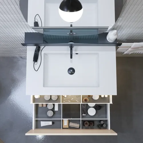 Stilfuld badeværelse inspiration med beige vaskeskab med inderskuffe, overskab, åben reol, oval spejl med belysning, matchende pendler, hylde under spejlet, og væghængt toilet. Vægge med lyse, aflange fliser.
