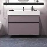Badeværelse med skrå vægge inspiration, med badeværelsesmøbler i lilla med elegante rammefronter, flot ovalt spejl med lampe, smuk og praktisk hylde, samt lillamalet væg og gråt sildebensgulv, der giver et elegant og moderne udtryk.